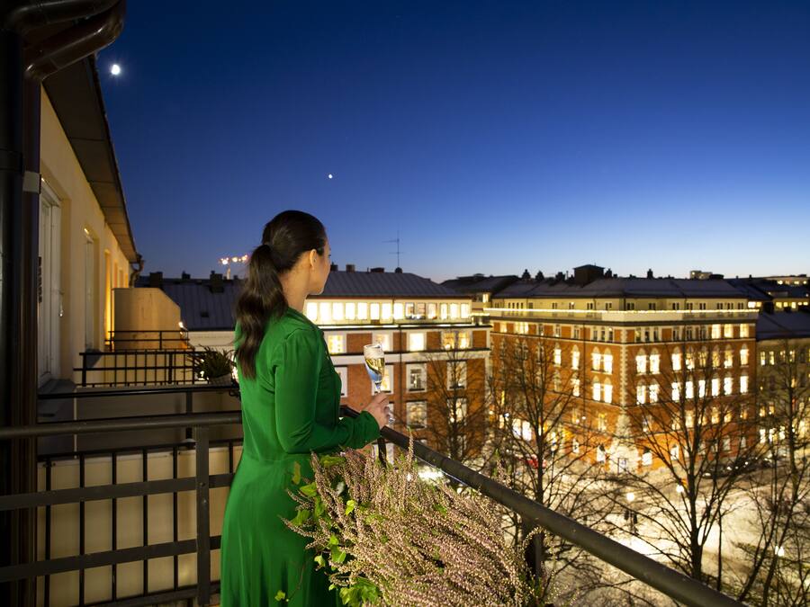 Una mujer con un vestido verde está de pie en un balcón con vista a un paisaje urbano nocturno.