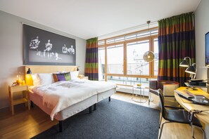 A hotel room with a large bed, a desk with a chair, a small table, and a window with curtains.