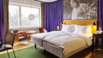 A hotel room with a large bed, a chair, a small table, and a window with curtains.