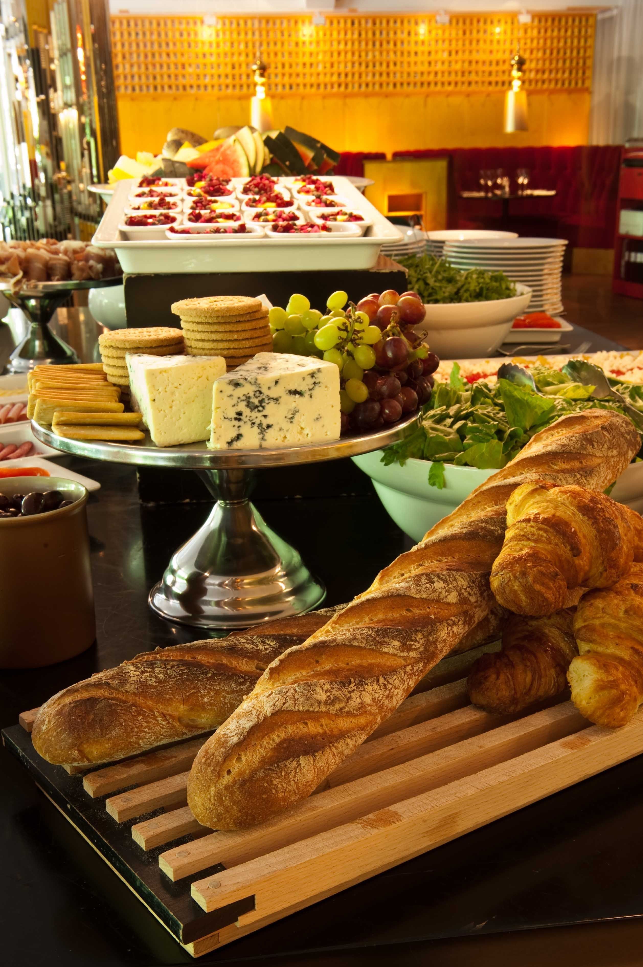 A buffet with various cheeses, crackers, grapes, and bread.