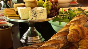 A buffet with various cheeses, crackers, grapes, and bread.
