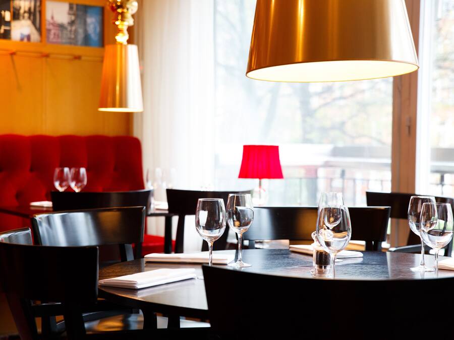 Un interior de restaurante con una mesa redonda dispuesta para comer, asientos tapizados en rojo e iluminación colgante.
