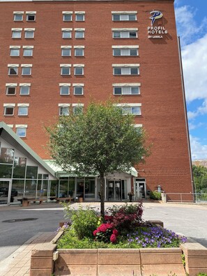 A hotel with a red brick facade, a large tree in front, and a sign for 'Profile Hotels by Ligula'. - ProfilHotels Nacka (Nacka)