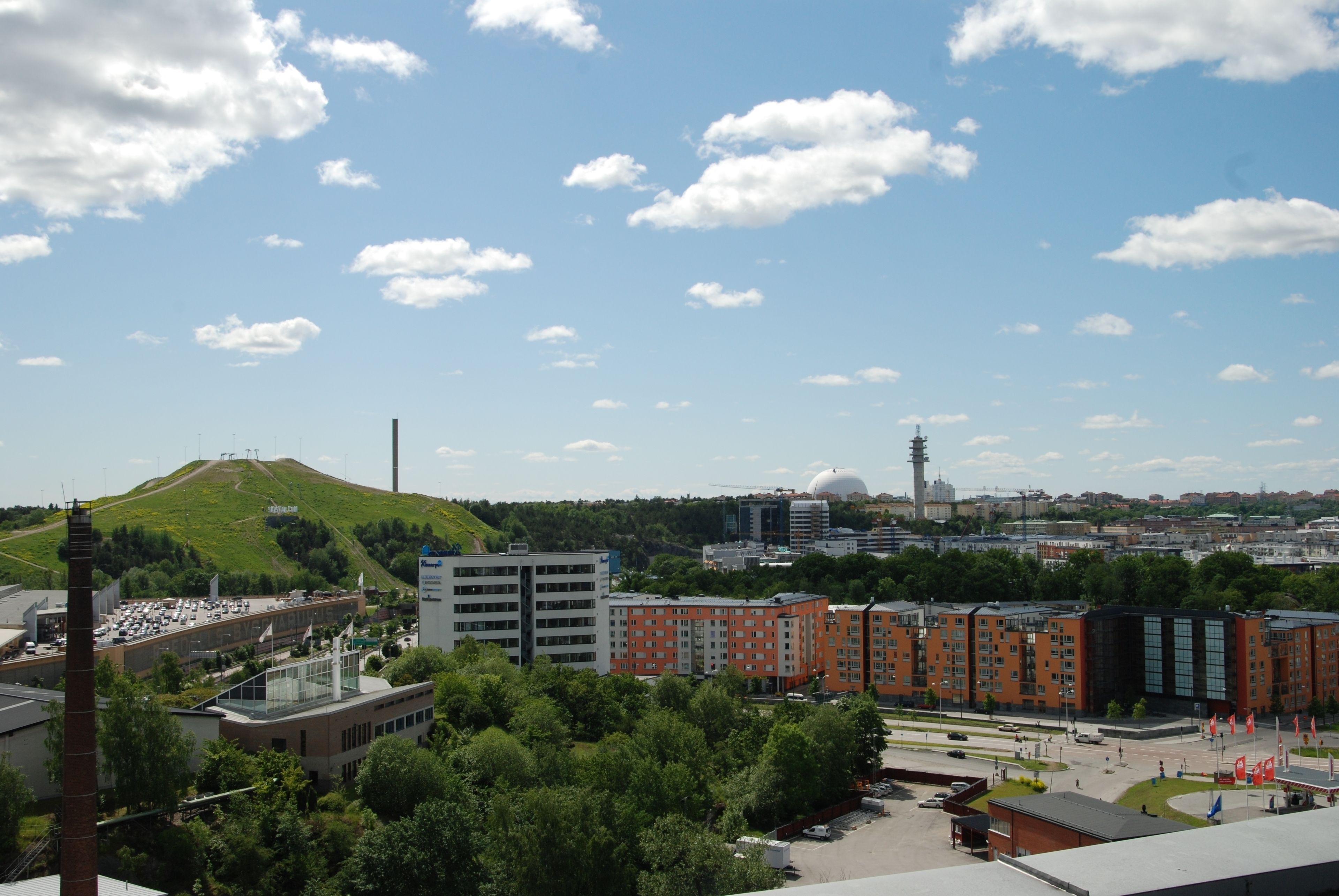 Un paysage urbain avec une colline bien visible, des bâtiments modernes et une tour qui se profile à l’horizon.