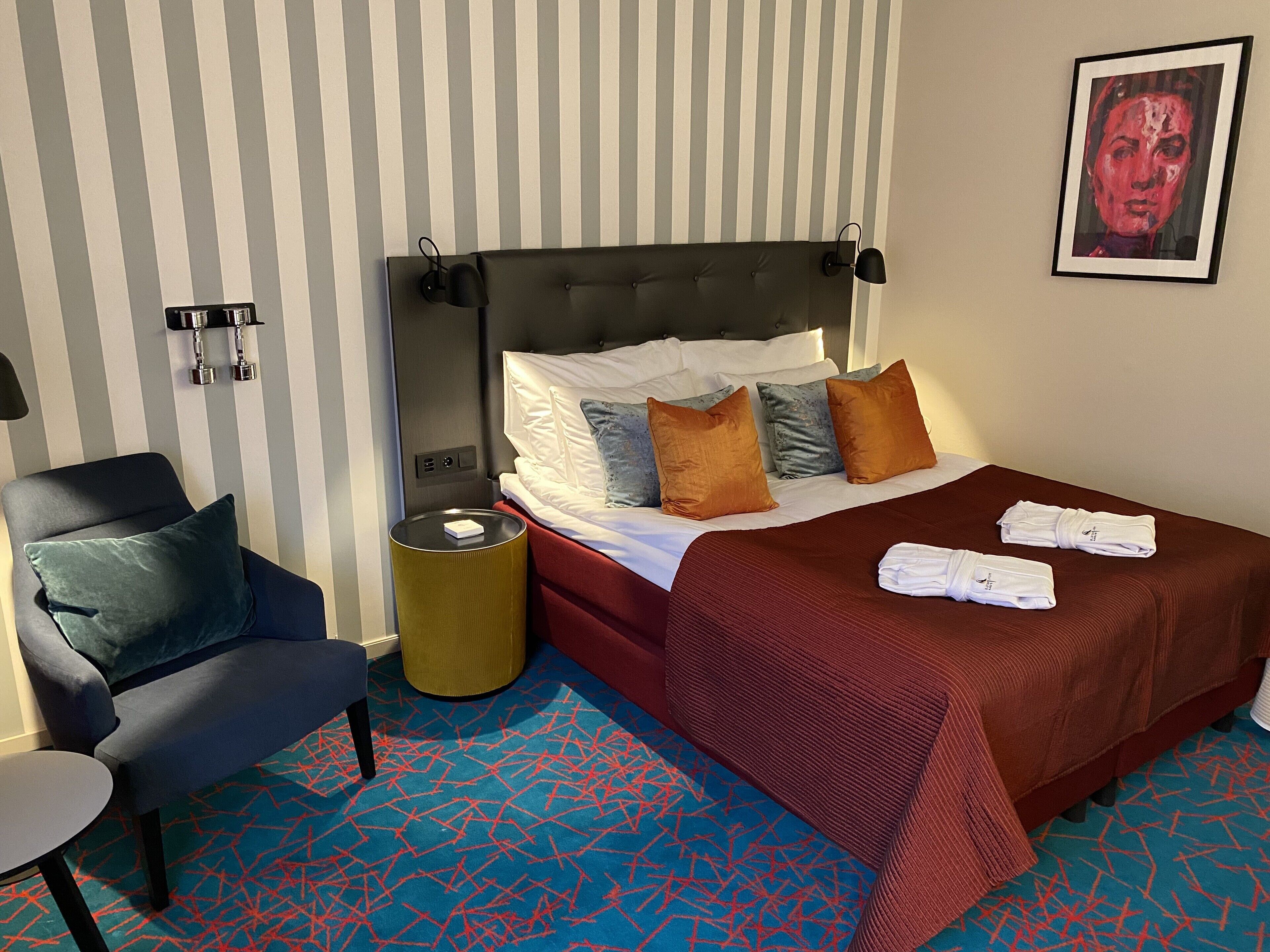 A hotel room with a bed, a chair, a bedside table, and a lamp.