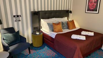 A hotel room with a bed, a chair, a bedside table, and a lamp.