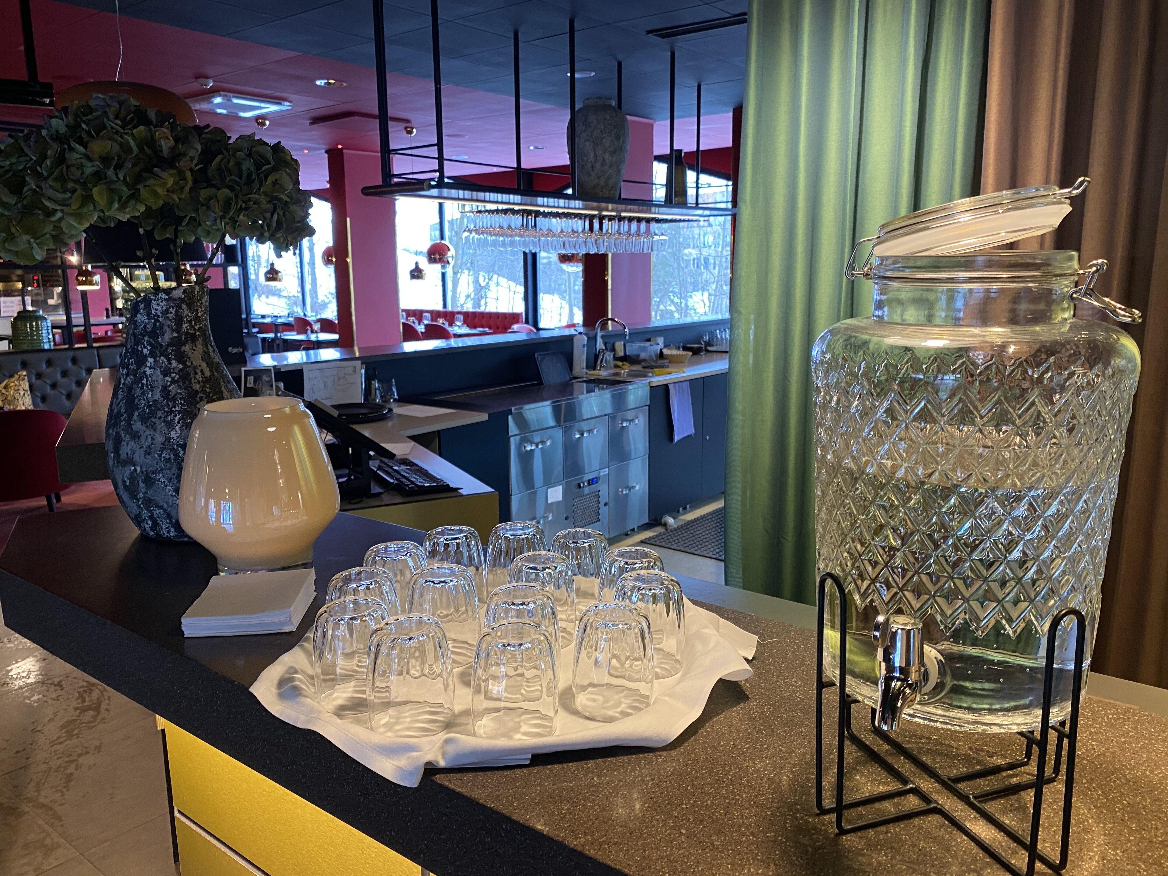 A bar area with a large crystal punch bowl and multiple glasses on a tray, a vase, and a bar counter with a sink and various items.
