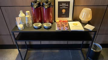 En frukostbuffé med kaffemaskiner, skålar, äpplen, muffins och en inramad meny.