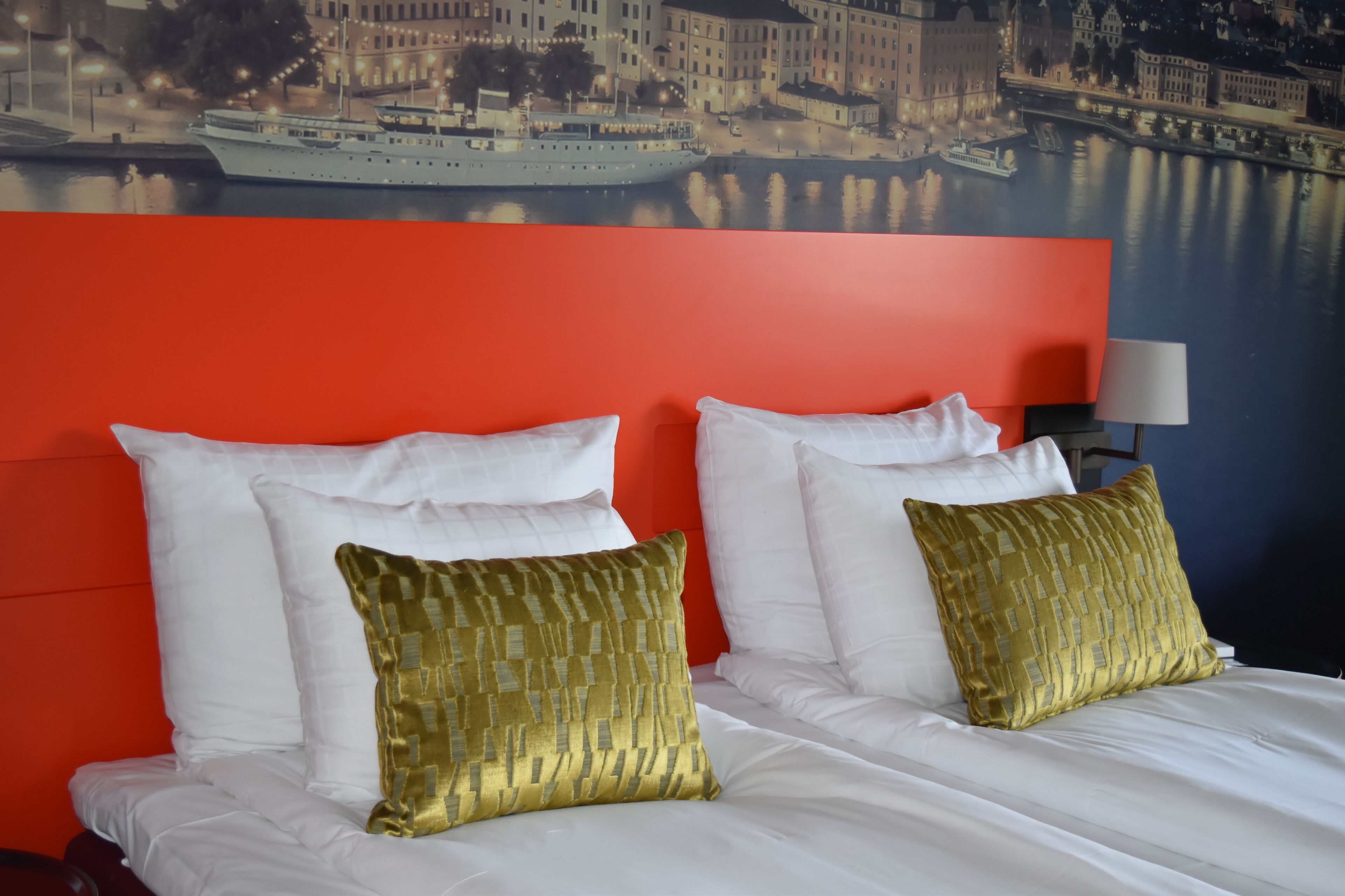 A hotel room with a large bed, two white pillows, and a red accent wall.