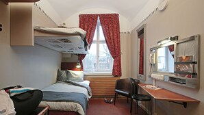 Habitación de hotel pequeña con una cama litera, un escritorio con silla, una mesita y un espejo.