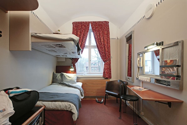 Habitación de hotel pequeña con una cama litera, un escritorio con silla, una mesita y un espejo.