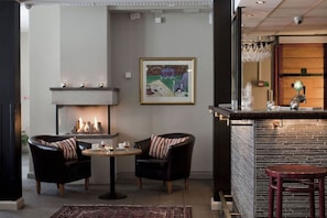 Un área de bar con chimenea, dos sillones y una mesa redonda.