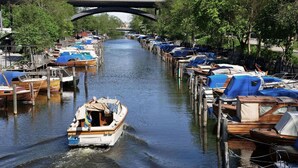 Un canal bordeado por barcos amarrados a ambos lados, con un puente al fondo y una embarcación navegando en el agua.