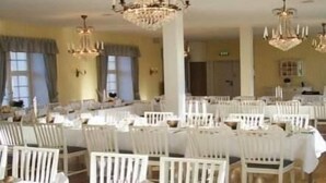 Un comedor con sillas y mesas blancas, candelabros y ventanas amplias.