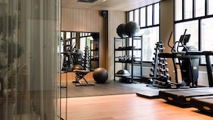 Un gimnasio moderno con equipamiento de ejercicio, amplias ventanas y suelo de madera.