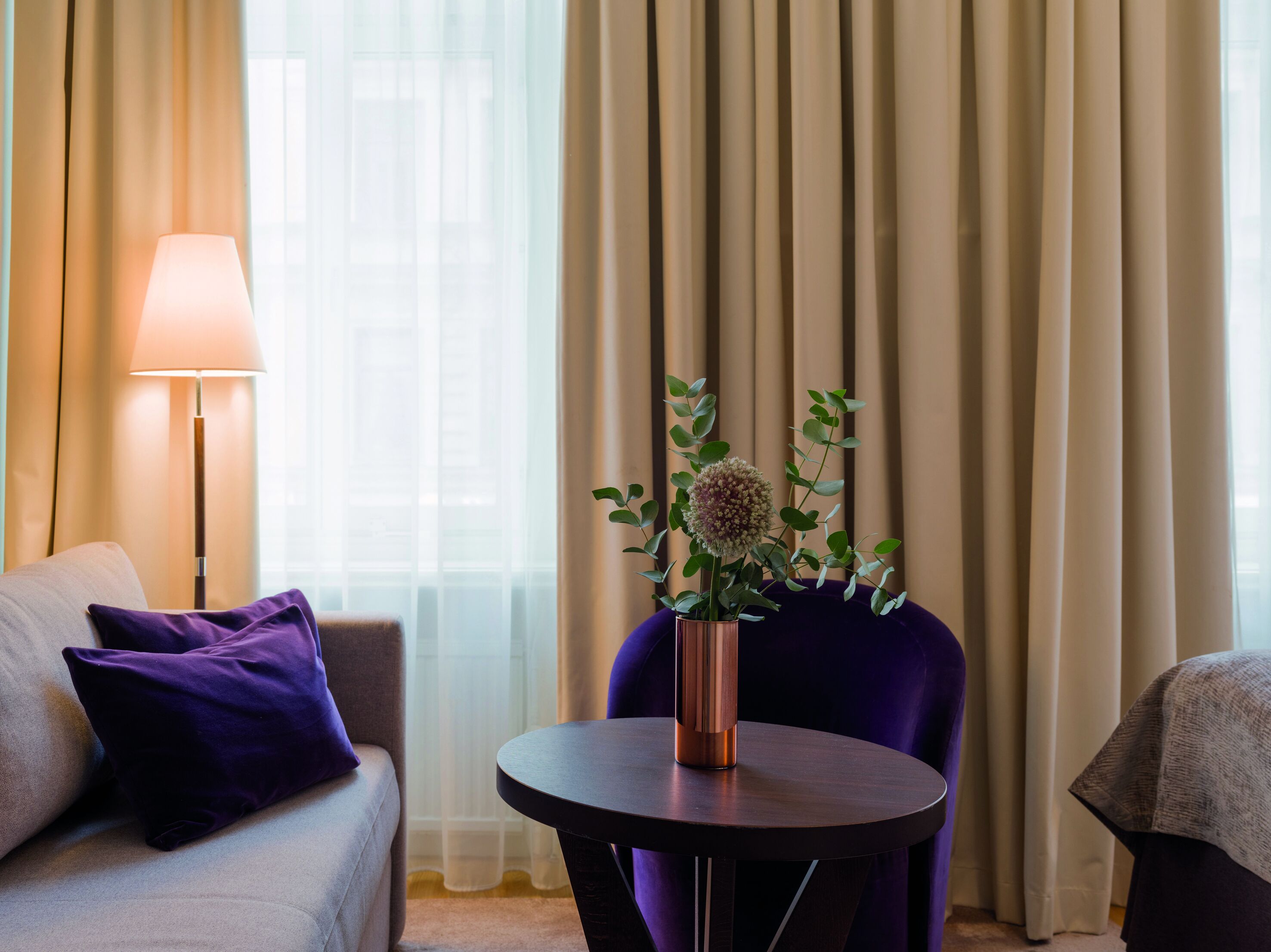 Ein modernes Hotelzimmer mit einer Couch, einem runden Tisch, einer Lampe und einer Vase mit Blumen.