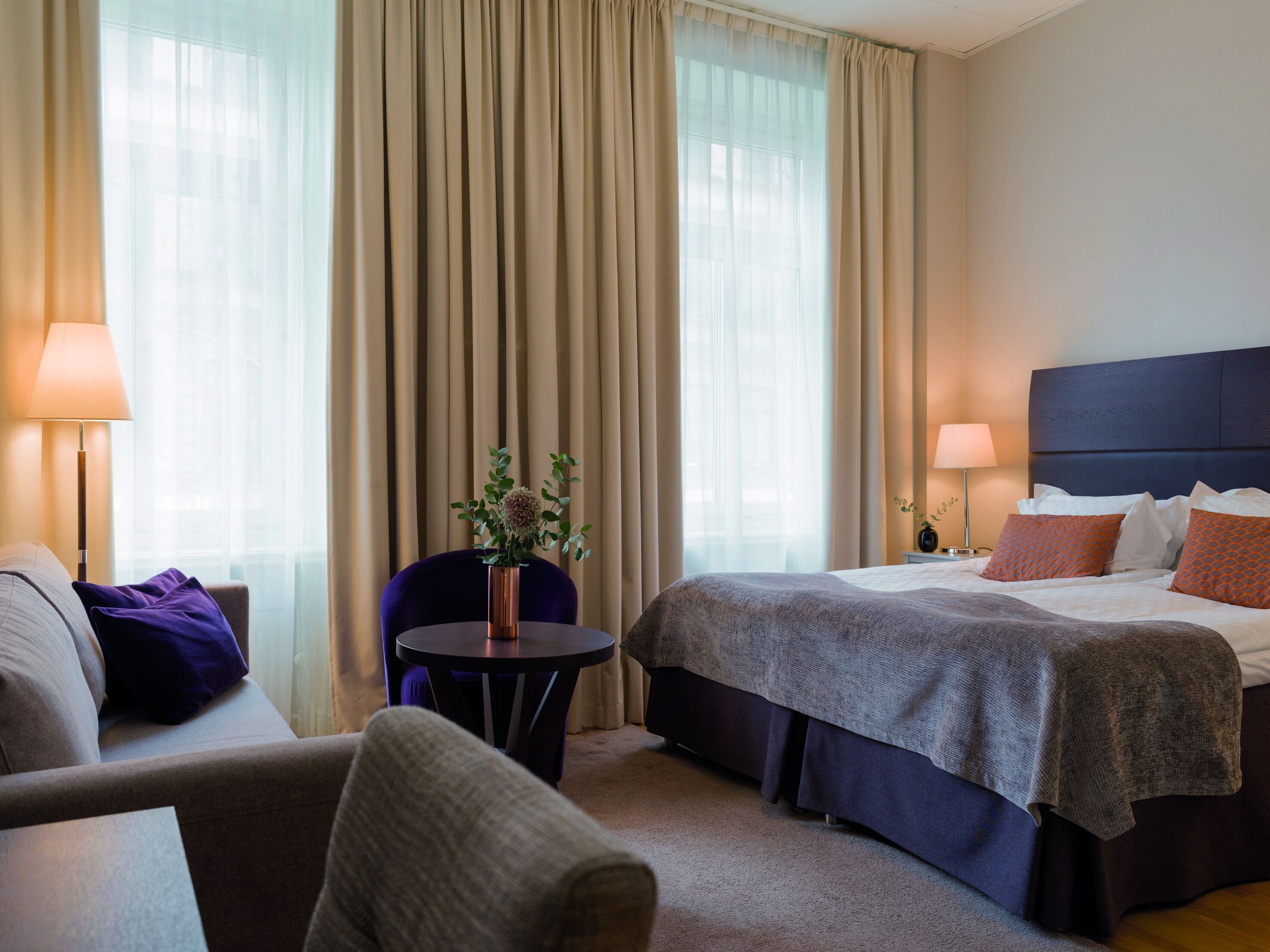 Et hotelværelse med en seng, en stol, et lille bord og en lampe.