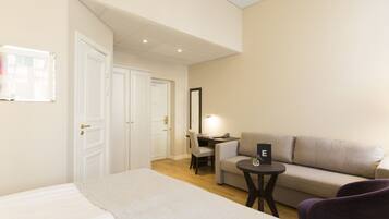 Une chambre d’hôtel comprenant un lit, un canapé, une petite table, un bureau avec une chaise et un miroir.