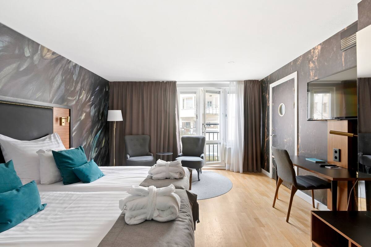 Ein modernes Hotelzimmer mit einem großen Bett, zwei Sesseln, einem Schreibtisch und Balkonblick.