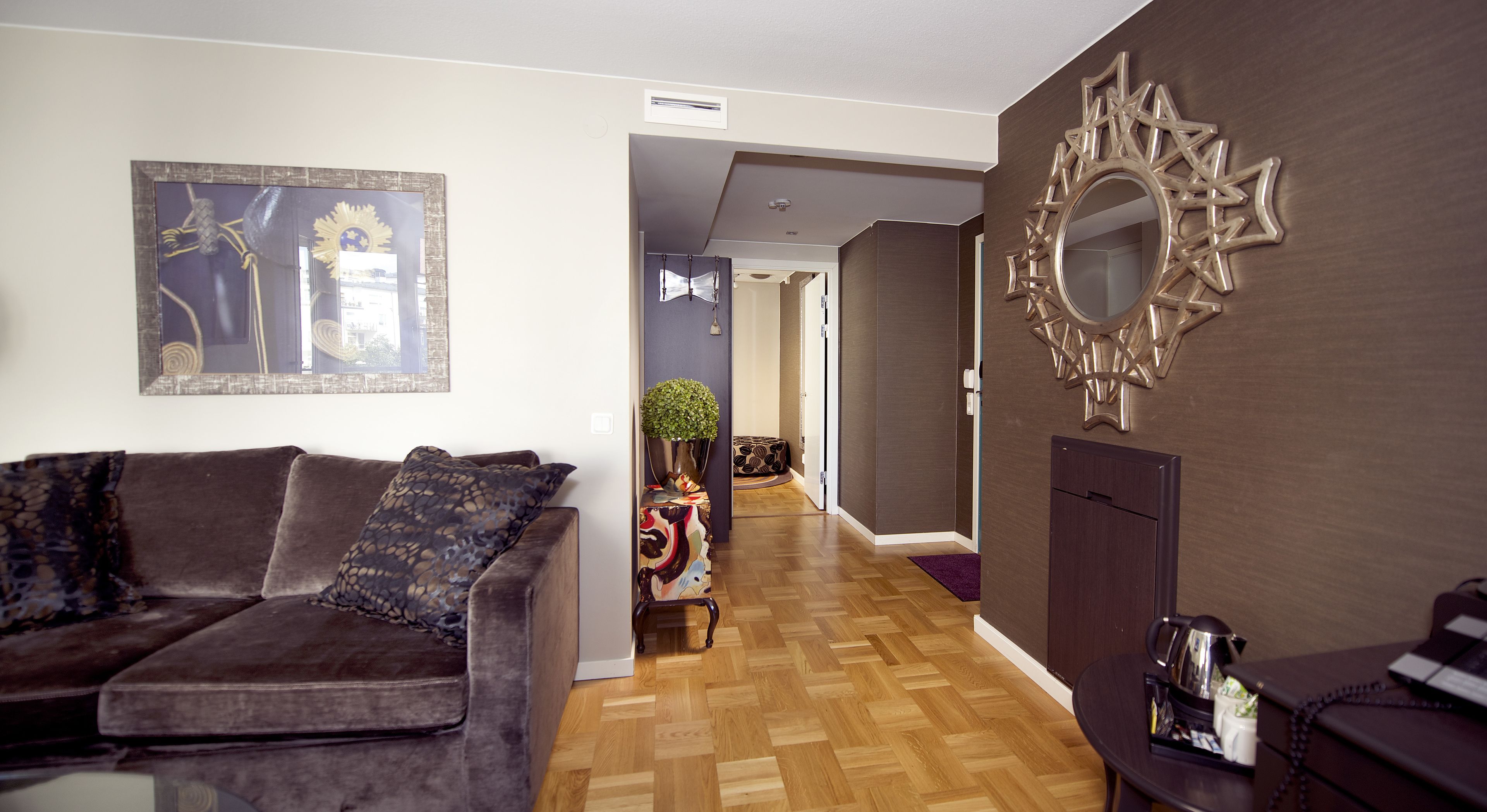 Un soggiorno moderno con un divano marrone scuro, uno specchio decorativo e un pavimento in legno.