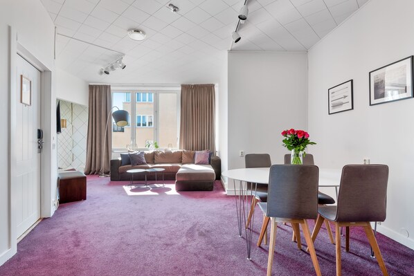 A modern living room with a purple carpet, a sofa, a dining table with chairs, and a window with curtains. - Home Hotel Tapto (Stockholm)