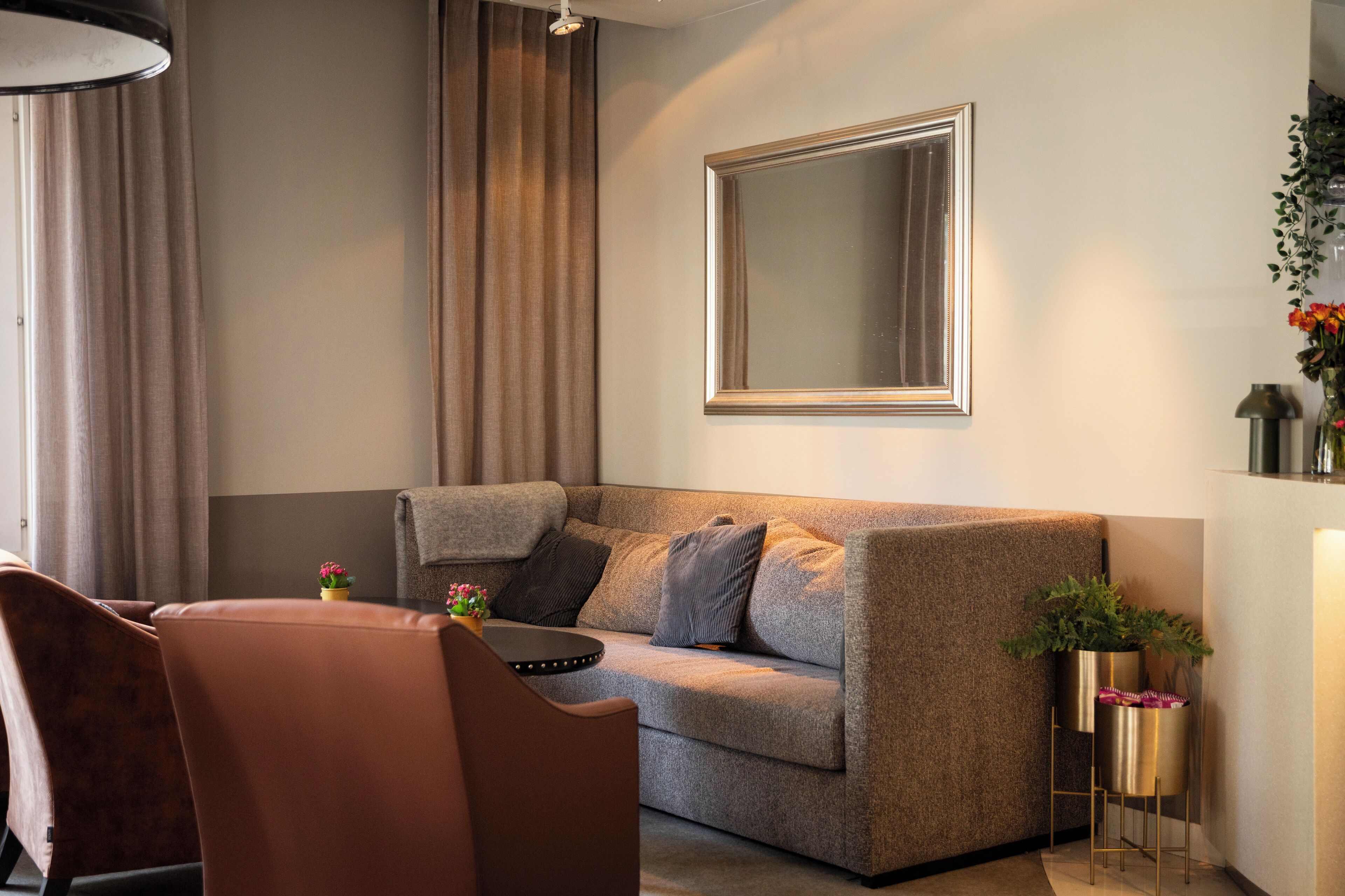 Un salon moderne avec un canapé gris, un fauteuil marron, une petite table sur laquelle est posée une plante, et un grand lampadaire.
