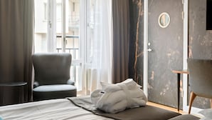 Hotellihuone, jossa on sänky, tuoli, kylpytakki, pieni pöytä ja ovi.