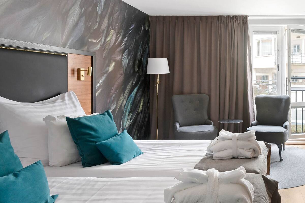 Ein Hotelzimmer mit Bett, zwei Stühlen, einem Schreibtisch, einem Fernseher und Blick ins Freie.