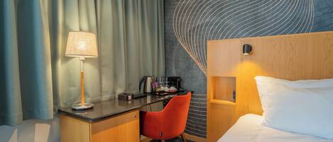 Habitación de hotel con cama, escritorio, silla, lámpara y una pared con diseño ondulado.