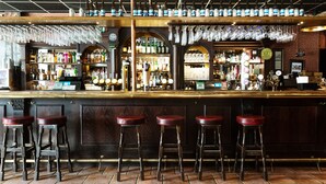 Een bar met houten krukken, flessenrekken en glazen die aan het plafond hangen.