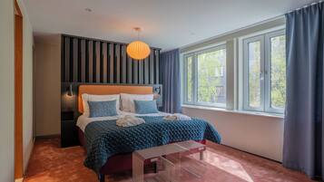 Ein modernes Schlafzimmer mit einem großen Bett, einem Nachttisch, einer Bank, einer Hängelampe und einem Fenster mit Vorhängen.