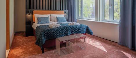 Ein modernes Schlafzimmer mit einem großen Bett, einem Nachttisch, einer Bank, einer Hängelampe und einem Fenster mit Vorhängen.