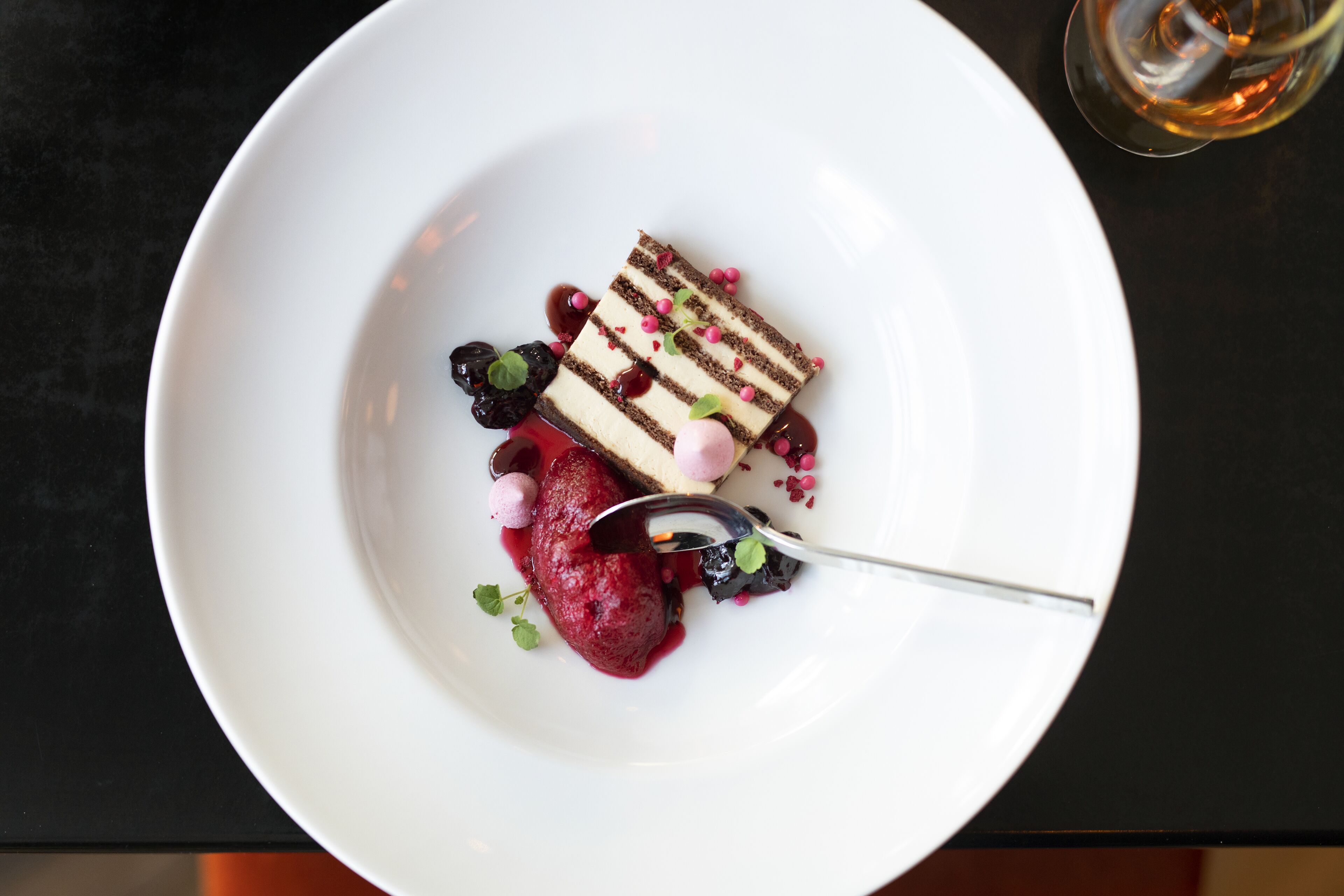 A white plate with a slice of layered cake, berries, and a spoon.