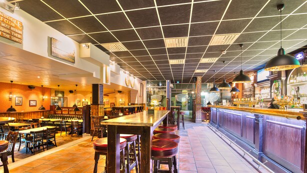 Een restaurant met een lange bar, meerdere tafels en zitjes.