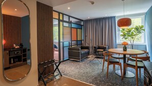 Een moderne kamer met een bank, een eettafel met stoelen, een spiegel en een raam met gordijnen.