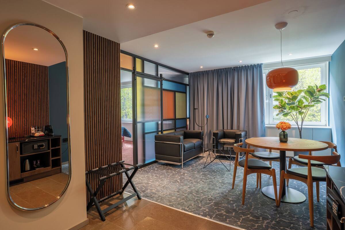 A modern room with a sofa, a dining table with chairs, a mirror, and a window with curtains.