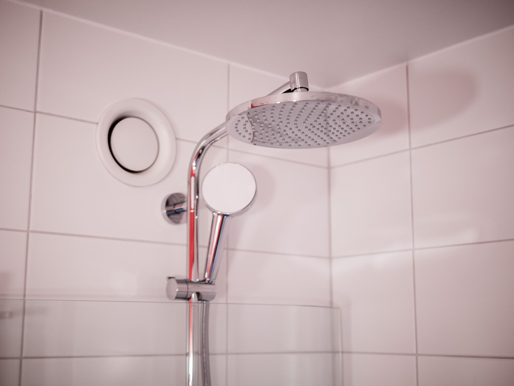 A shower with a handheld showerhead and a wall-mounted circular mirror.