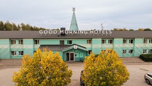 Ett motell med en grön fasad, ett centralt torn och en skylt med texten ”GOD MORGON, HOTELL”.