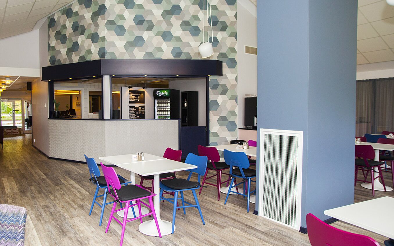 Un comedor interior moderno con sillas y mesas coloridas, una barra con un menú y una pared estampada.
