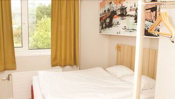 A bedroom with a bed, a radiator, a window with curtains, and a painting on the wall.