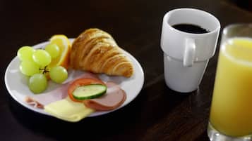 Un plato con jamón, queso, tomates, pepinos y uvas, un croissant, una taza de café y un vaso de jugo de naranja sobre una mesa.