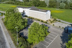 Un hotel grande de diseño moderno, con un estacionamiento y un campo verde al fondo.