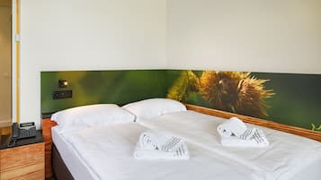 Une chambre d’hôtel avec un lit, deux serviettes blanches, une table de chevet avec un téléphone et un mur vert orné d’une plante.