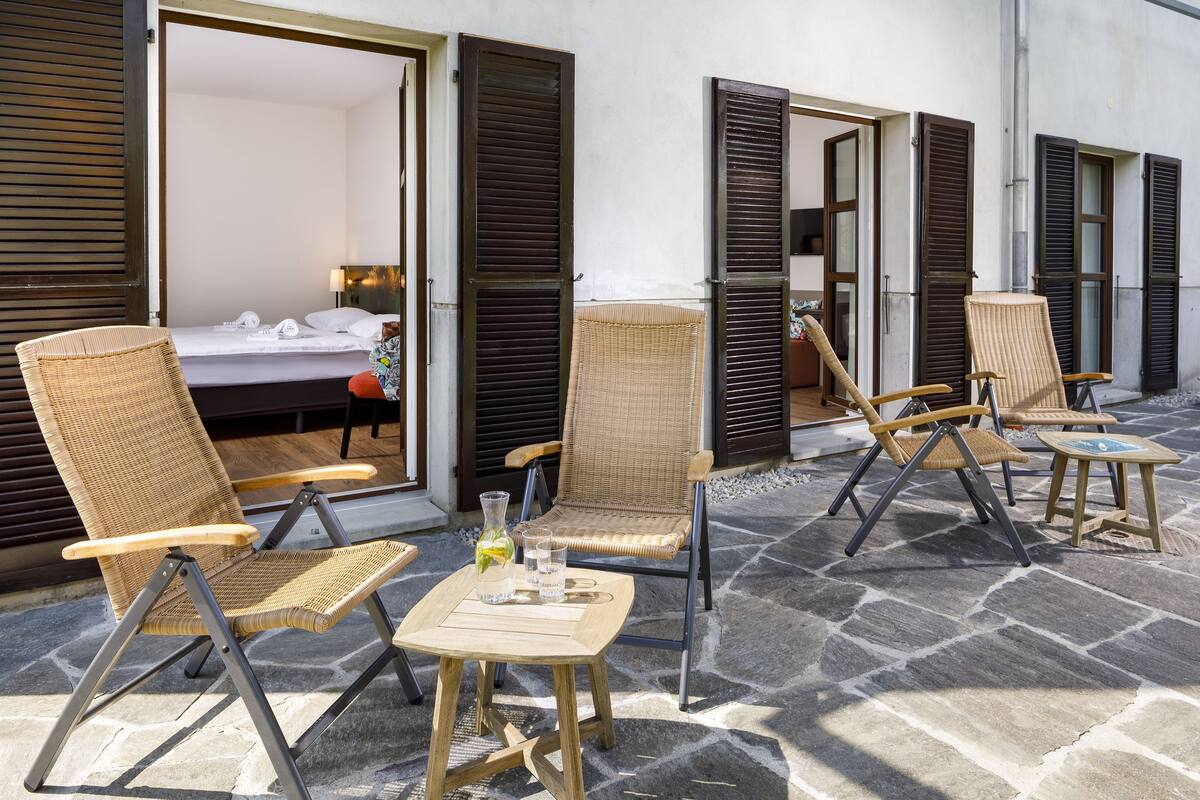 Une chambre d’hôtel avec un lit, une chaise en osier et une petite table sur laquelle se trouvent un verre et une bouteille.