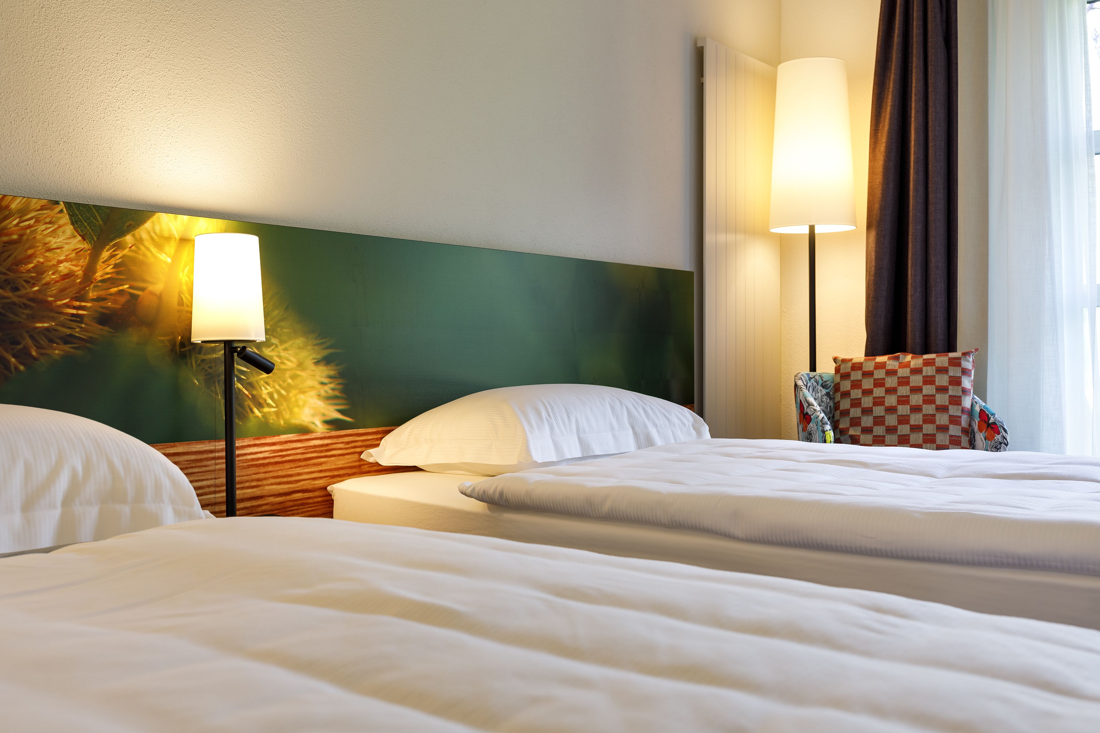 A hotel room with two beds, a large wall mural, a standing lamp, and a checkered pillow.