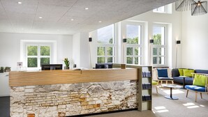 A modern reception area with a brick wall design, large windows, and a seating area with a sofa and chairs. - Hotel Bellinzona Sud Swiss Quality (Bellinzona)