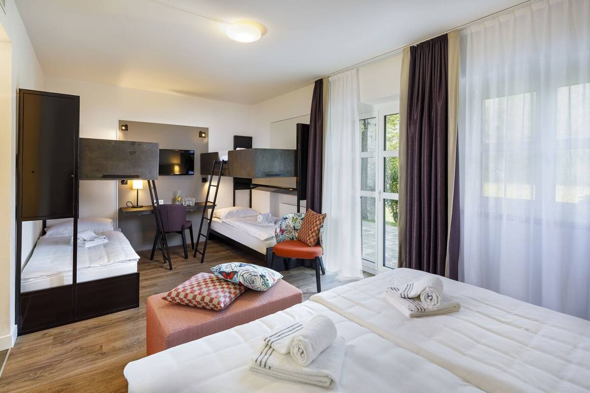 Une chambre d’hôtel avec deux lits, un bureau, une chaise, une télévision et une grande fenêtre avec des rideaux.