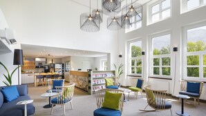 A spacious lobby with modern furniture, a reception desk, and large windows offering views of greenery. - Hotel Bellinzona Sud Swiss Quality (Bellinzona)