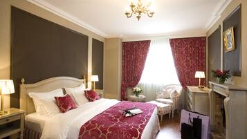 A well-appointed hotel room with a large bed, a chandelier, a fireplace, and a seating area with a chair and a small table.