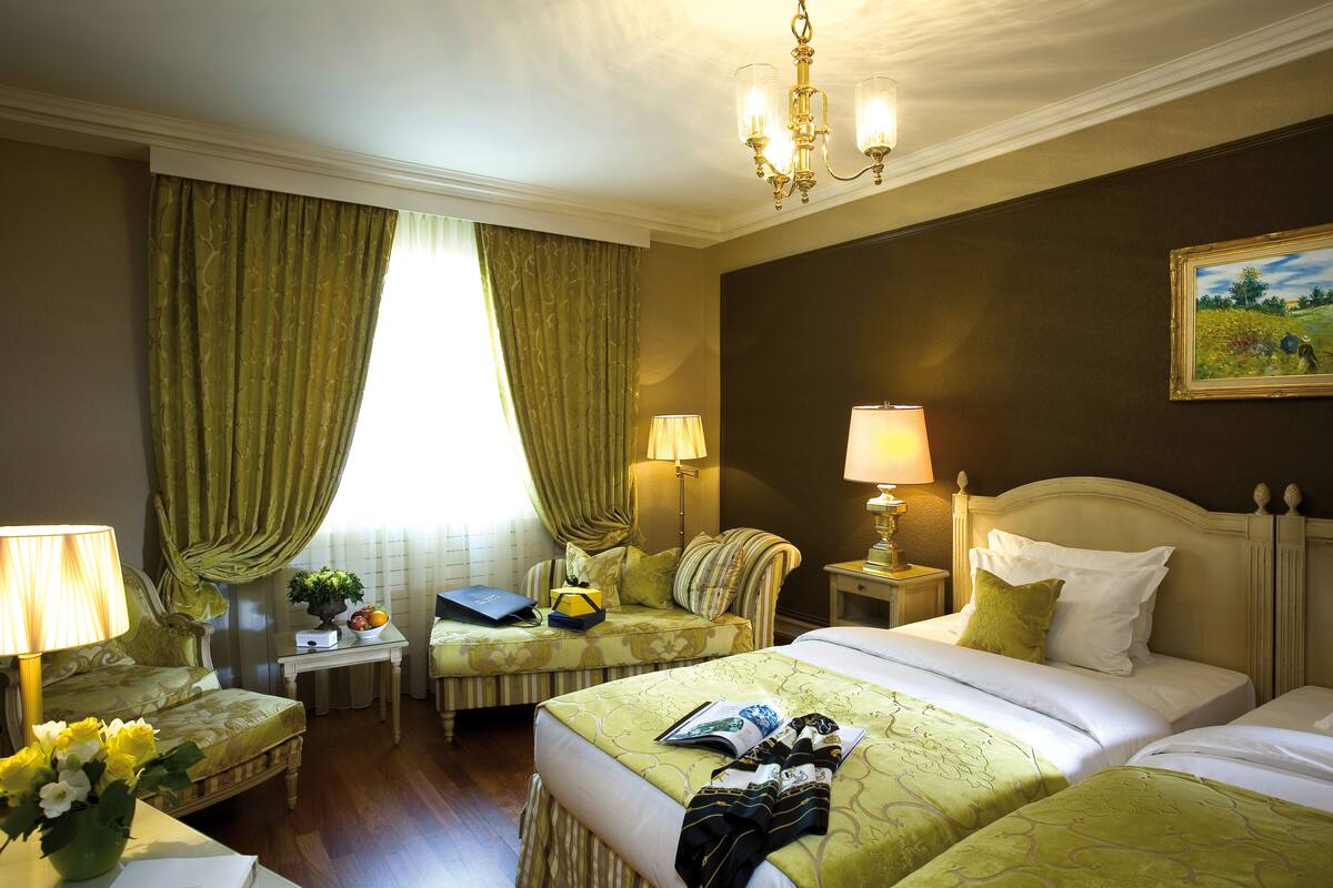 A hotel room with two beds, a sitting area, and a window with curtains.